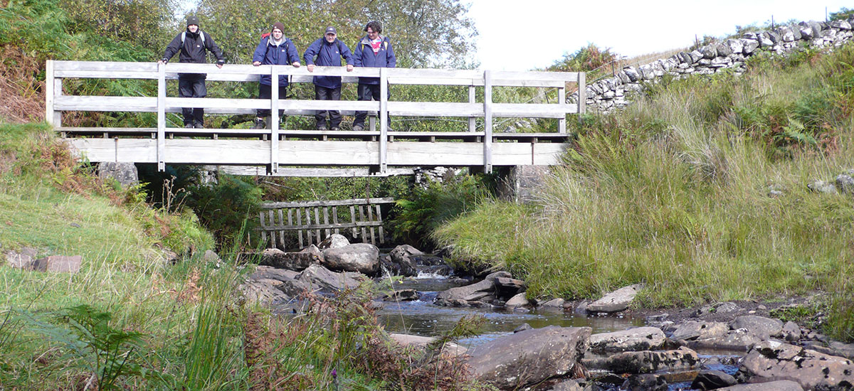 walkers on a DoE course with Mountainwise pasue on a bridge to enjoy the view a stream